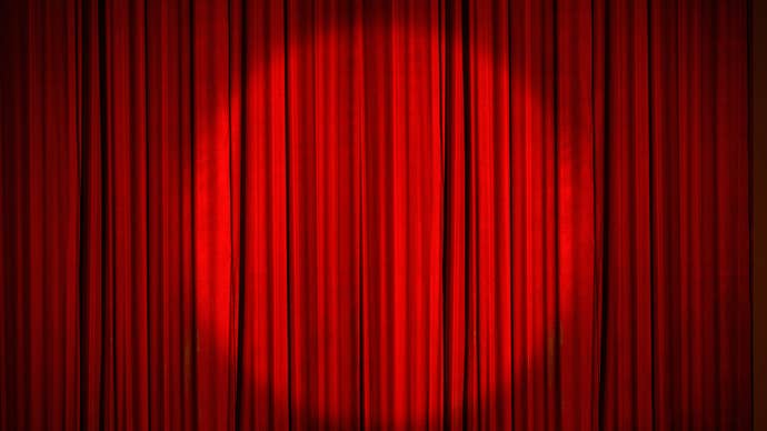 A red stage curtain, drawn, with a circular spotlight shining on the middle of it.