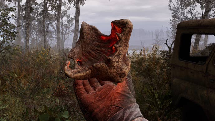 The player in Stalker 2 holds a glowing brown and red Artifact in their hand in a forest.