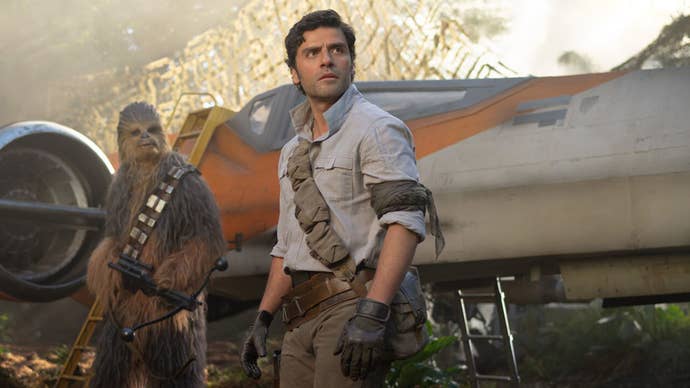 Poe Dameron is stood looking off at something concerned, Chewbacca in the background looking in the same direction in Star Wars.