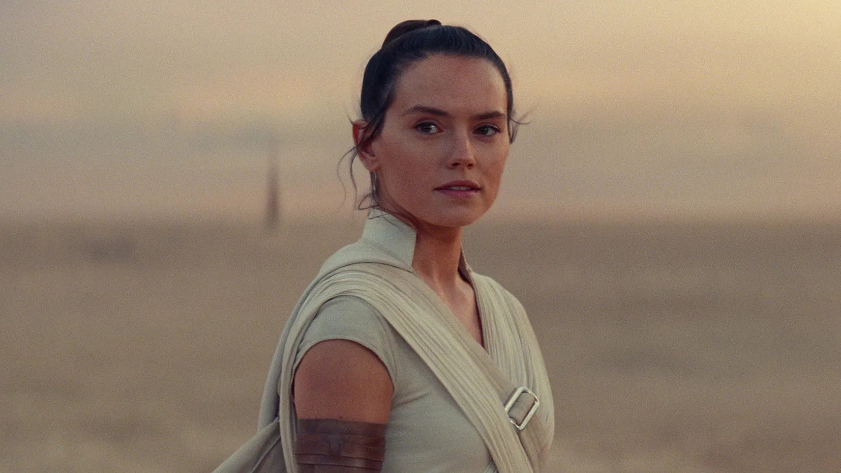 Rey in Star Wars: The Rise of Skywalker, she's on a desert planet looking at something offscreen with a slight smile on her face. - 1