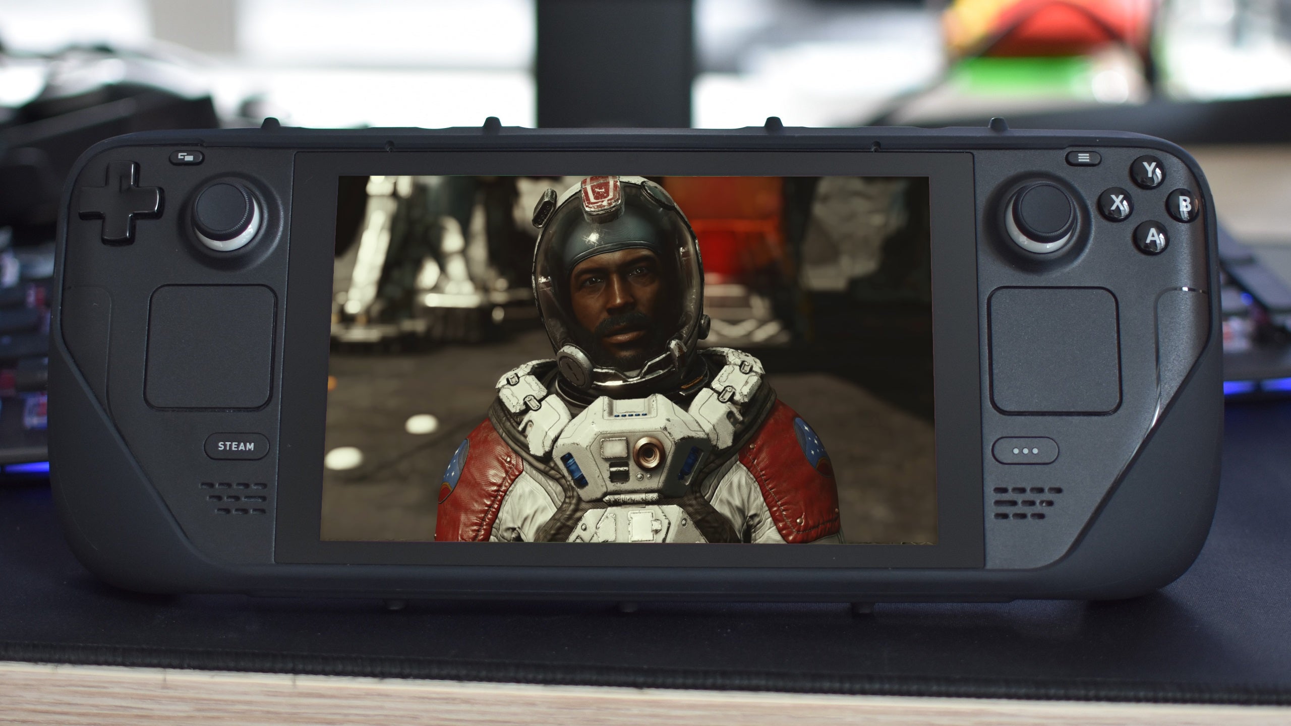 A photo of a Steam Deck propped up on a desk, with a Starfield screenshot superimposed over the Steam Deck&rsquo;s screen.