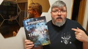 Paizo's Thurston Hillman posing with a copy of The Gap, Starfinder's April Fools joke book.
