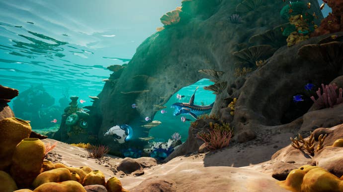 A Subnautica screenshot showing a colourful seabed and arching rocks in a turquoise ocean.