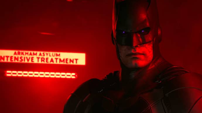 Close up of Batman with purple eyes, bathed in red light.