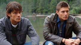 Jared Padalecki and Jensen Ackles sat in front of a lake in a scene from Supernatural.