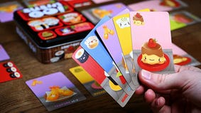 A hand holding a fan of Sushi Go! cards in front of several cards and the game box on a table