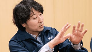 Photograph of Takuhiro Dohta of Nintendo, in dark blue Nintendo jumpsuit, explaining something with hands raised.