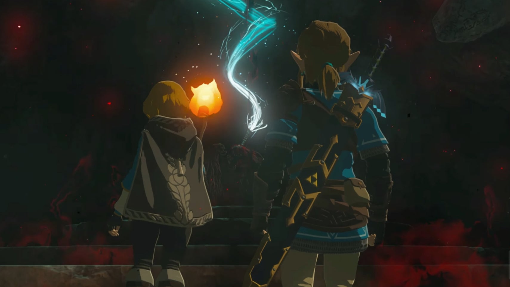 Zelda and Link are stood in a dark cave, a mummified corpse with a hand place on its chest, a glowing light eminating from the hand in Tears of the Kingdom. - 1