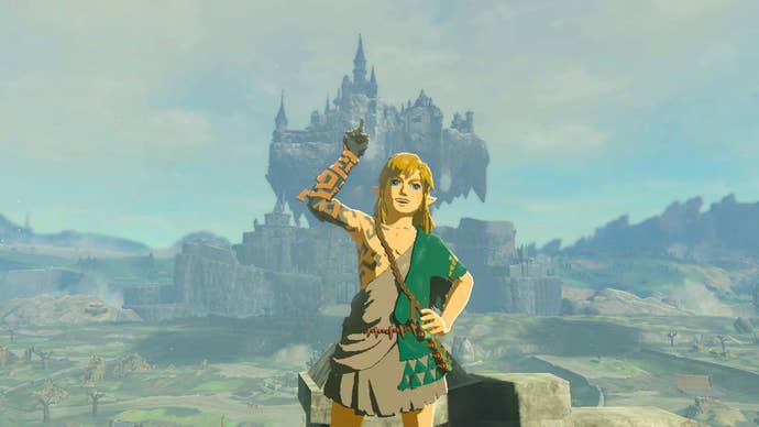 Zelda: Tears of the Kingdom screenshot showing Link smiling for the camera, pointing upwards, Hyrule Castle floating in the distance behind him.