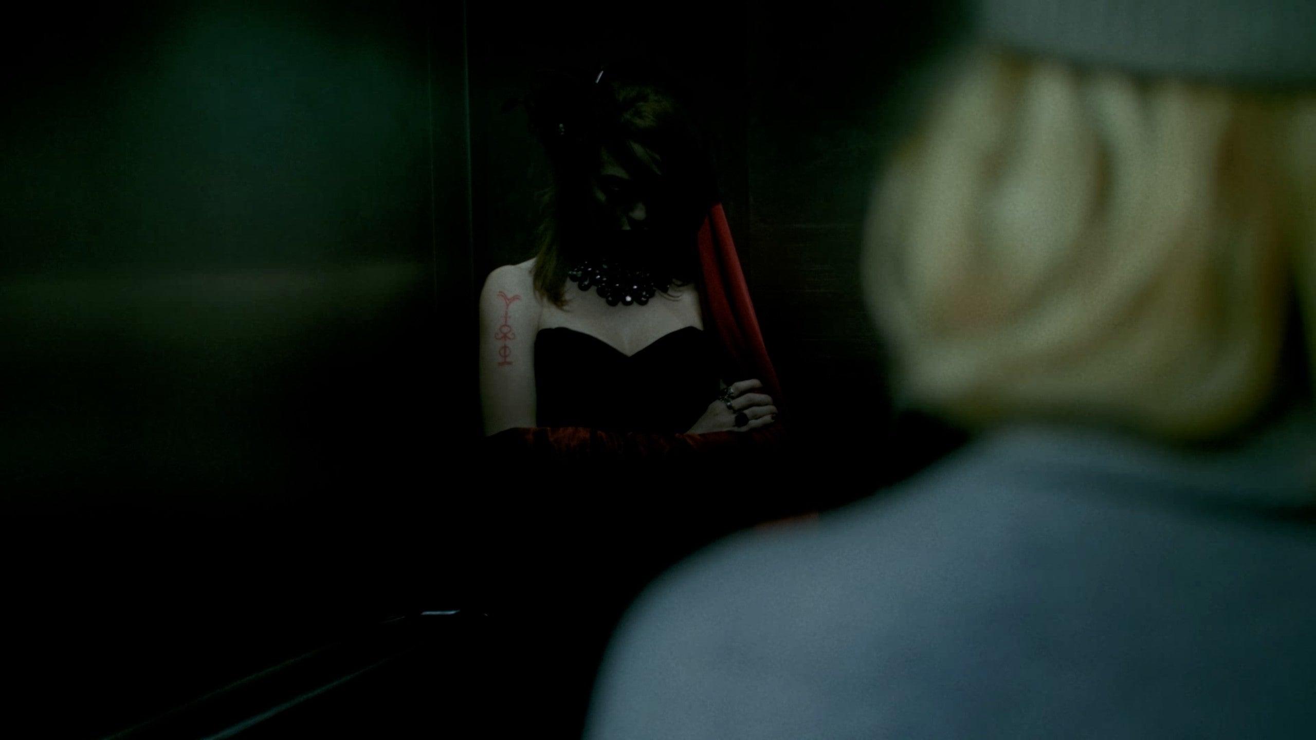 A live-action image of two characters standing in a darkened lift. One of the characters is barely visible.