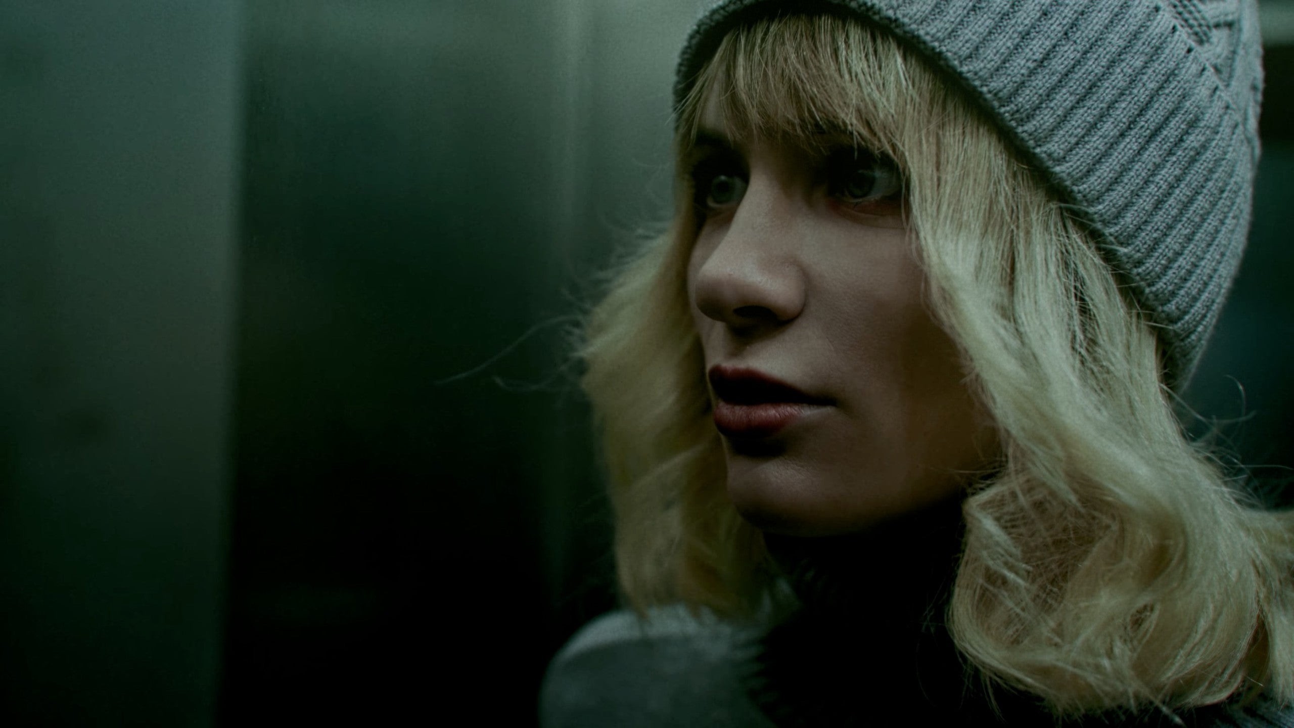 A blond feminine character in a live-action sequence stares intently at something off screen.