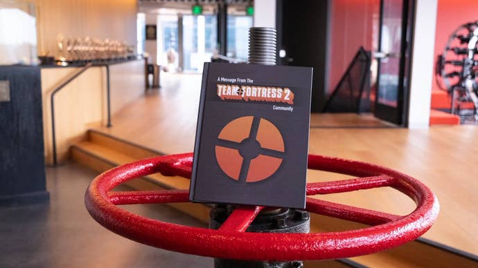 A photo of a large black hardback book titled “A message from the Team Fortress 2 community”, resting on a red valve wheel in developer Valve’s office lobby.