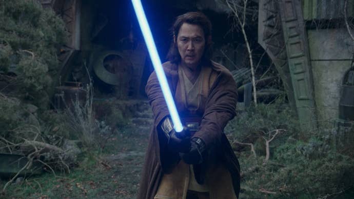 Sol, a Jedi with long hair, is stood in a fighting position, lightsaber lit in The Acolyte.