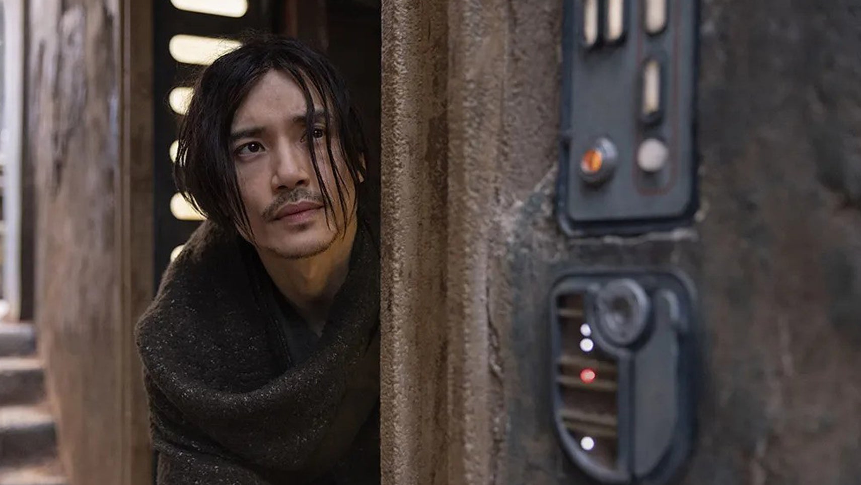 Manny Jacinto in The Acoylte, he's stood sheepishly in a doorway, messy hair covering his face. - 1