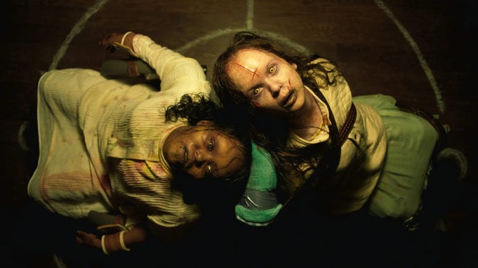 A still from The Exorcist: Believer showing two young girls that are possessed, they're leaning back towards each other looking up at the camera.