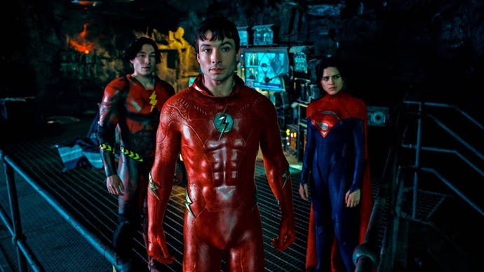 Two versions of The Flash, and Supergirl, stood in the Batcave in The Flash (2023).