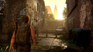 A screenshot from The Last of Us Part 2 showing a character walking through a derelict city street while the sun rises behind a steeple in the distance.
