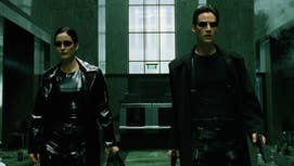 A still from The Matrix of Trinity and Neo walking through a corporate building, both in black leather trench coats and sunglasses on.