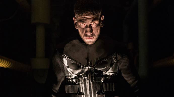 Jon Bernthal is stood as The Punisher in the show of the same name, he’s looking into the camera, wearing a military-like uniform with a skull on it.