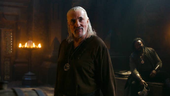 Kim Bodnia as Vesemir in The Witcher. He’s stood in a candlelit chamber, looking at something offscreen.