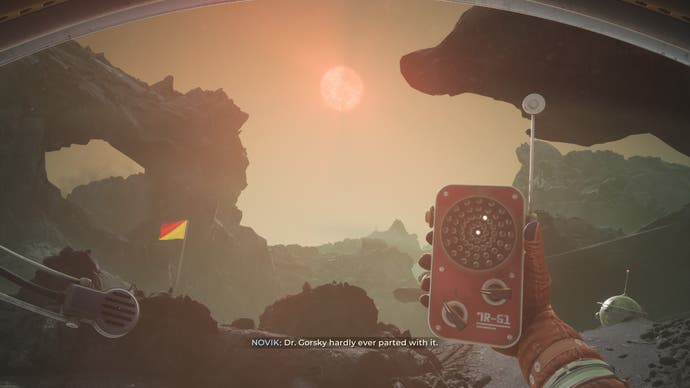 A screenshot from The Invincible, showing a first-person perspective of an astronaut character holding up a walkie-talkie like device locator and looking out at a rocky area with a low-hanging, orange sun in the sky before them.