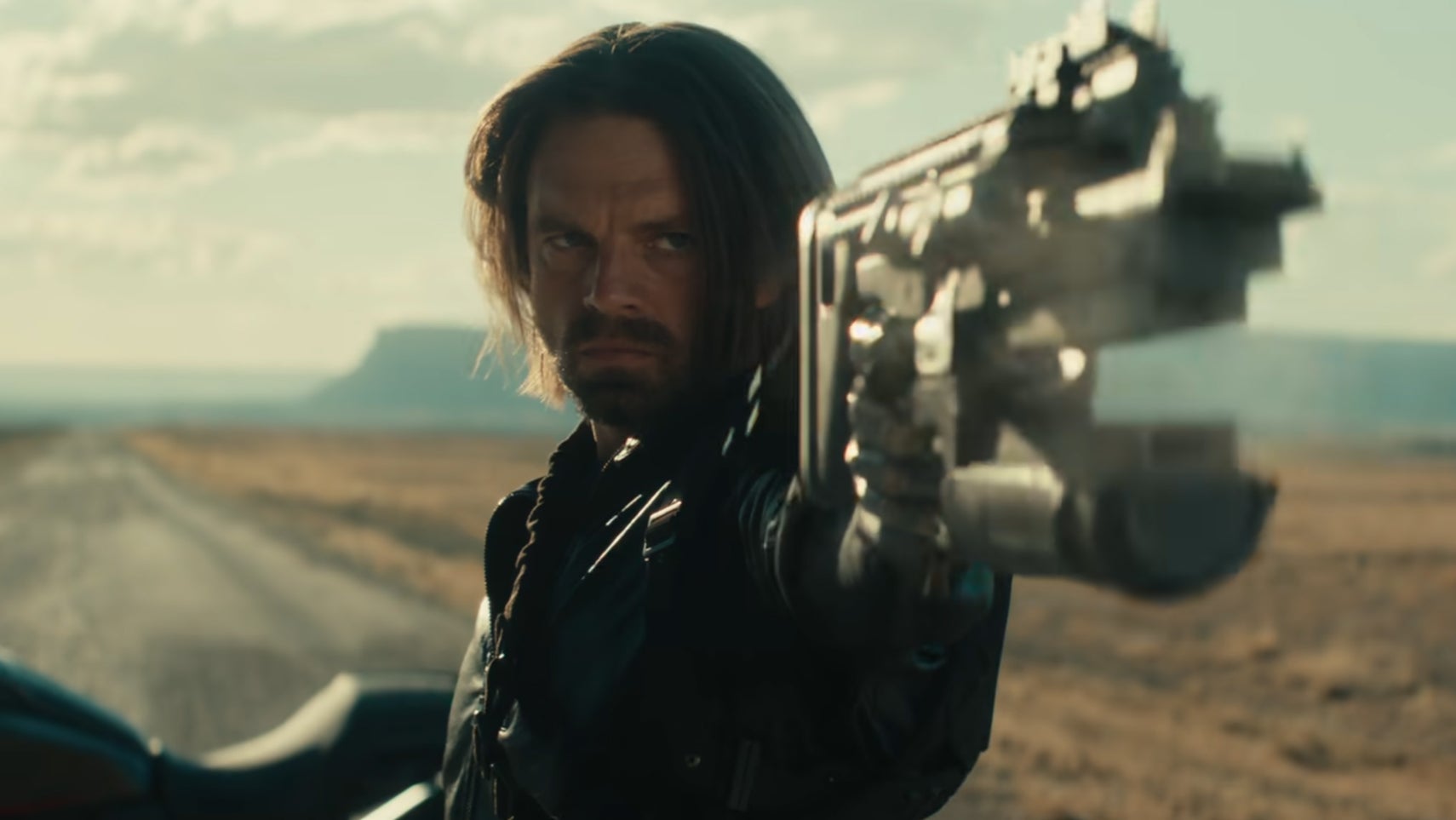 Bucky Barnes in Thunderbolts on a long stretch of road in the middle of nowhere, pointing a gun at something offscreen. - 1