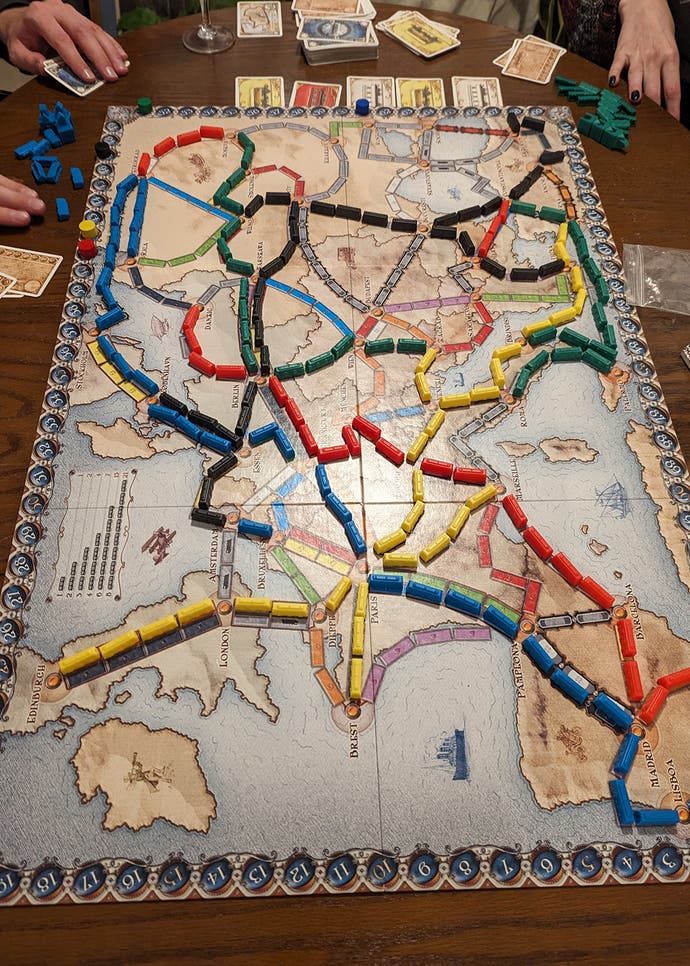A photo of the board game Ticket to Ride being played. It's a top-down image showing the game's map-like board, which has primary-coloured plastic trains snaking all around it.