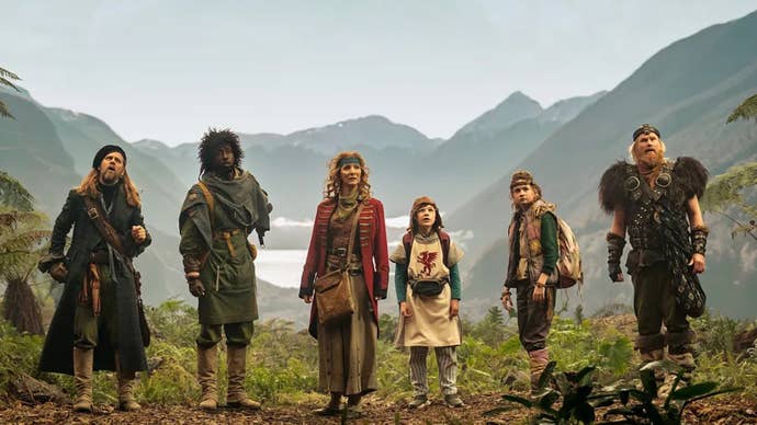 The main cast of the Time Bandits TV series stood in a line in a mountainous area all looking at something offscreen.