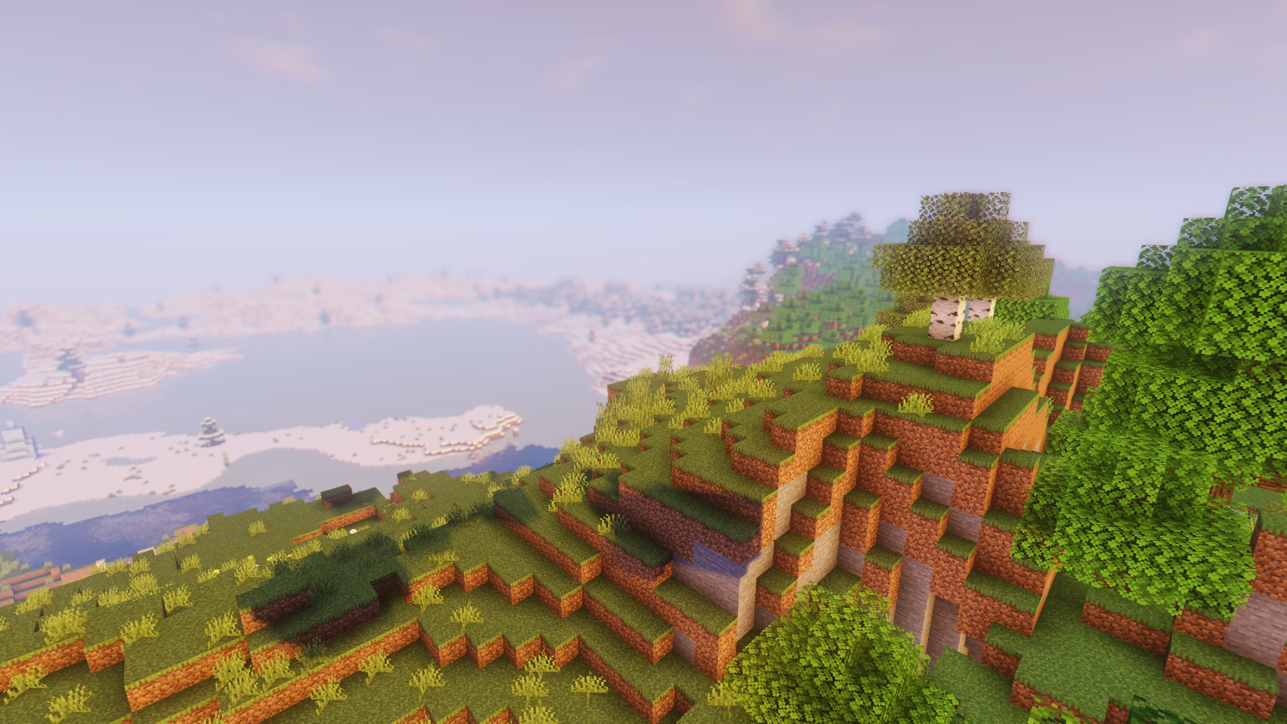 A Minecraft hill in the foreground, with a snowy landscape in the background and TME Shaders installed.