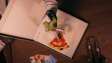 A shot from the Teenage Mutant Ninja Turtles: Empire City teaser trailer showing a top-down view of a pizza box, with Raphael's hand skewering the last slice of pizza with his sais.
