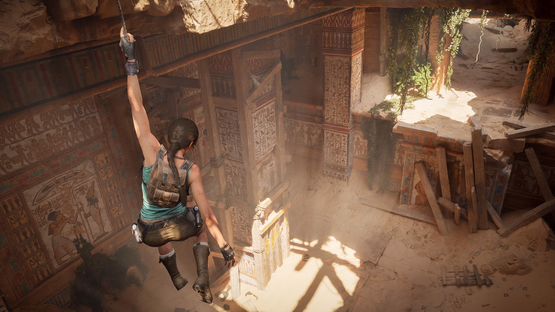 A white but tanned lady with a long brown plait hangs from a rope above a ruin of some kind. It's Lara Croft just... hanging around.
