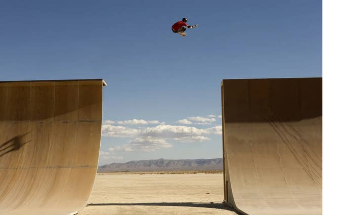 Tony Hawk flies between two huge quarter-pipe ramps in the desert, his red shirt agains tthe clear blue sky