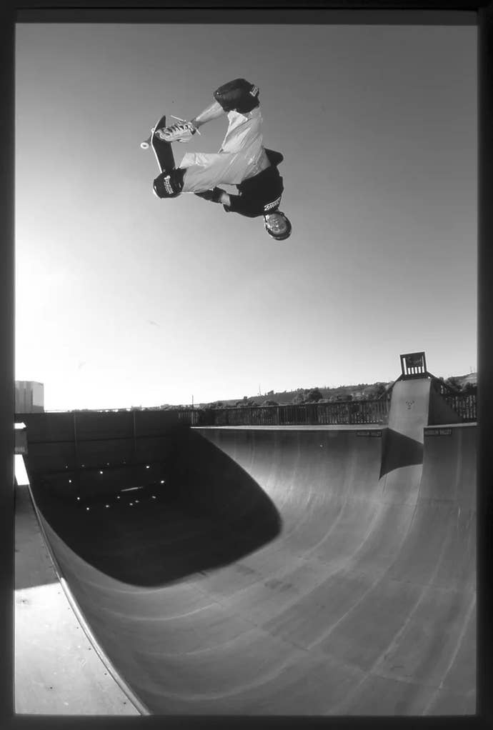In black and white, Tony Hawk flies upside-down over a half-pipe