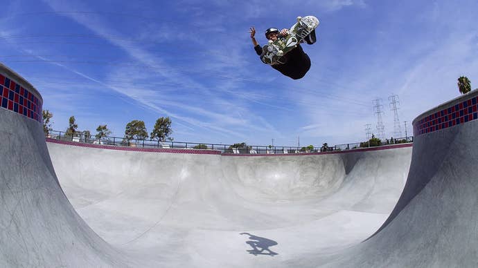 Photo of Tony Hawk, flying between two sides of a skate park basin, nothing but blue sky above and his lone shadow on the ground below