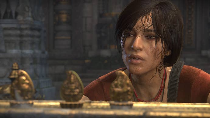 Uncharted heroine Chloe Frazer in close up, looking at a trio of golden-looking figurines on a ledge of some kind. She’s sweaty and dirty, and concentrating.