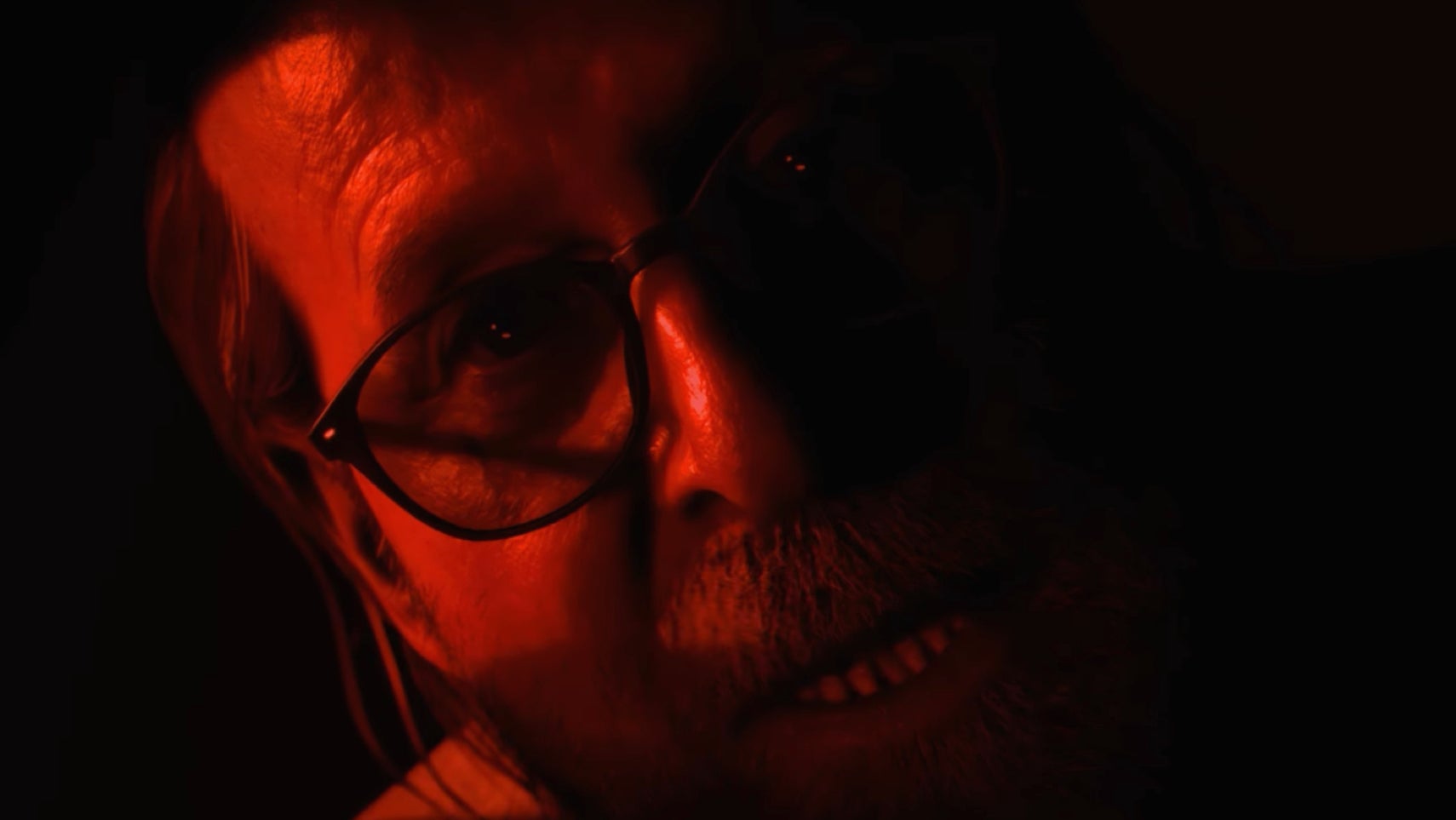 Until Dawn 2 screenshot showing a bearded Peter Stormare, returning as Dr. Hill, bathed in red light.