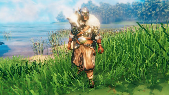 A player in Valheim stands on a Meadows coast and faces the camera wearing Wolf armour.