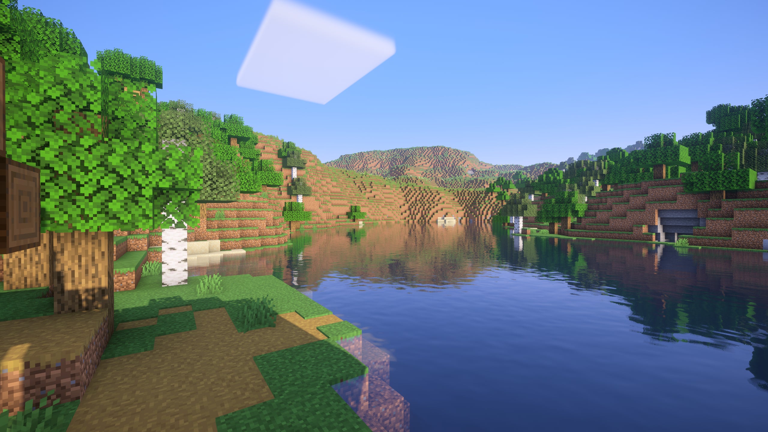 A screenshot of a river in Minecraft, with some trees on either side of the bank and a hill in the distance, taken using Vanilla Plus shaders.