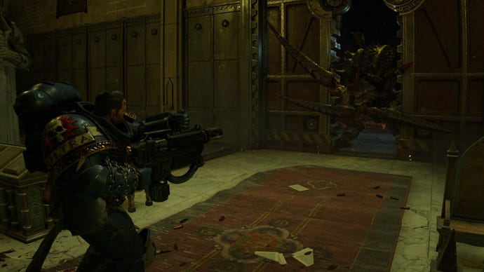 Titus points his weapon at a carnifex while it forces its way into the room.