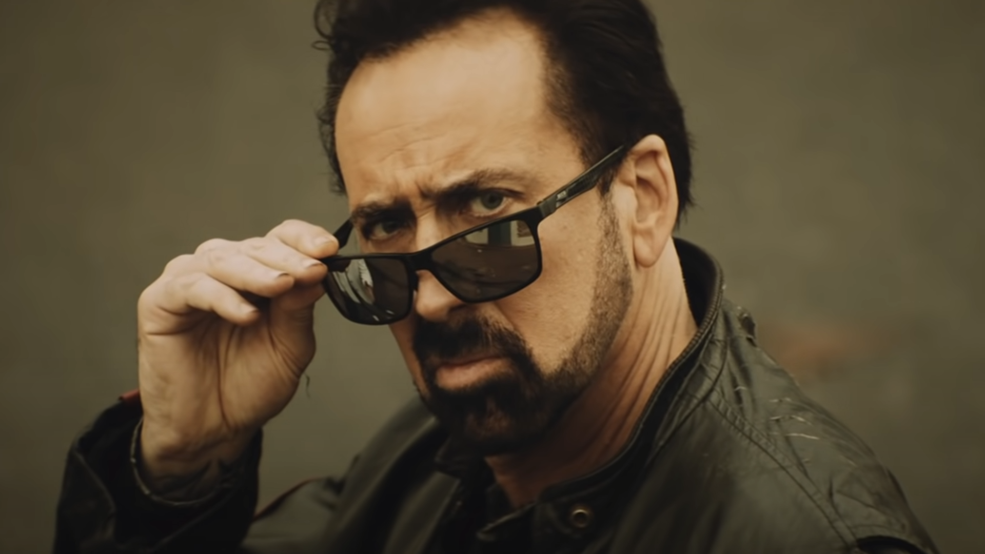 Nicolas Cage removes his sunglasses slightly while looking past the camera in Willy&rsquo;s Wonderland