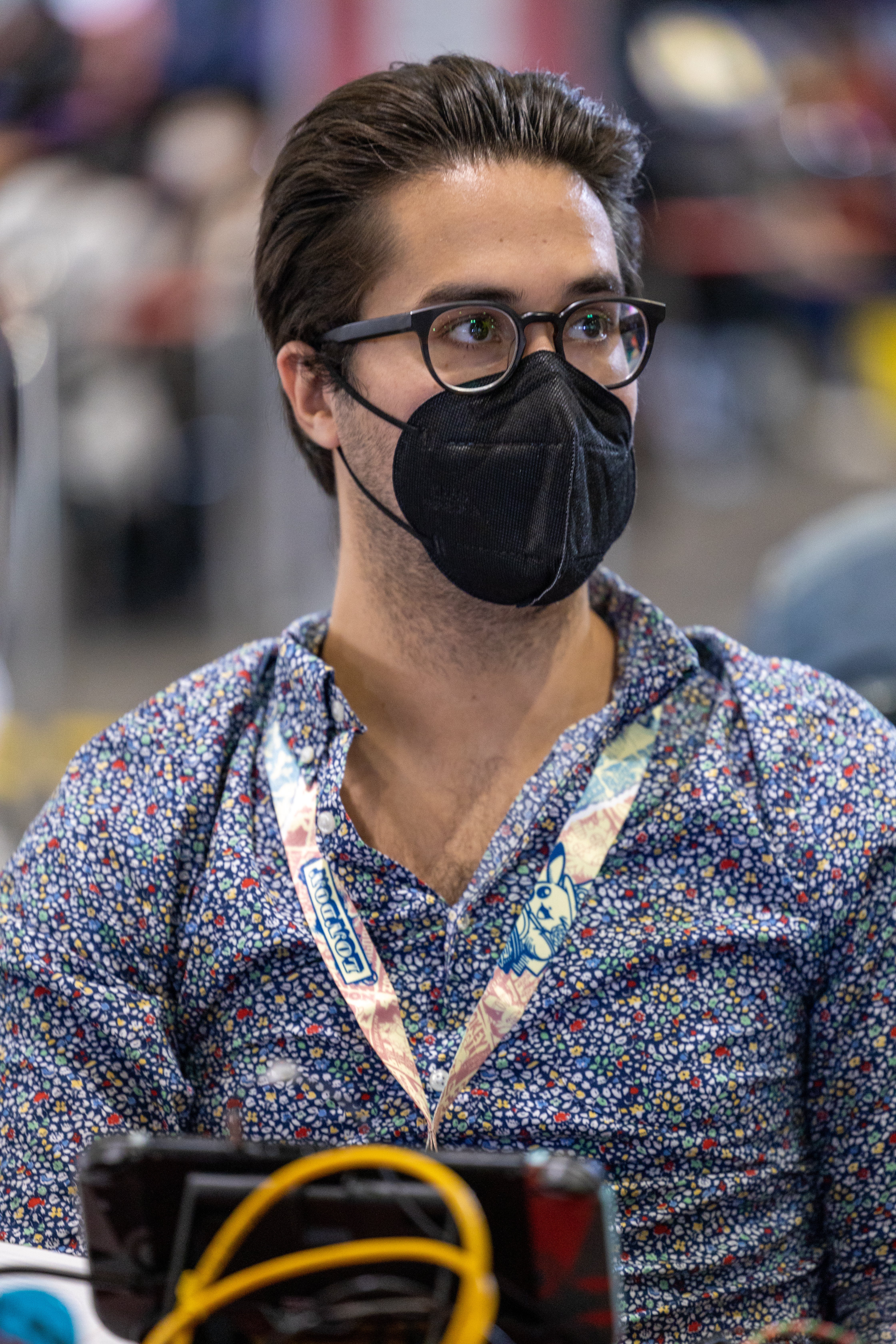 A portrait photograph of Pokemon champion Wolfe Glick looking off to the camera&rsquo;s right. He&rsquo;s nicely groomed, with hair brushed back and a patterned shirt on. A black face mask and glasses cover much of his face.