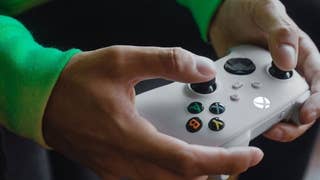 Close up of a white Xbox controller behind held by someone in a green top