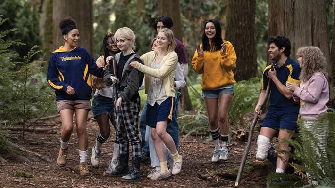 Some of the cast of Yellowjackets crowding around Natalie, who is holding a gun looking proud of herself.