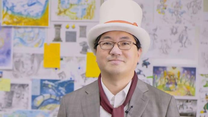 Yuji Naka in a white top hat in front of a board of designs