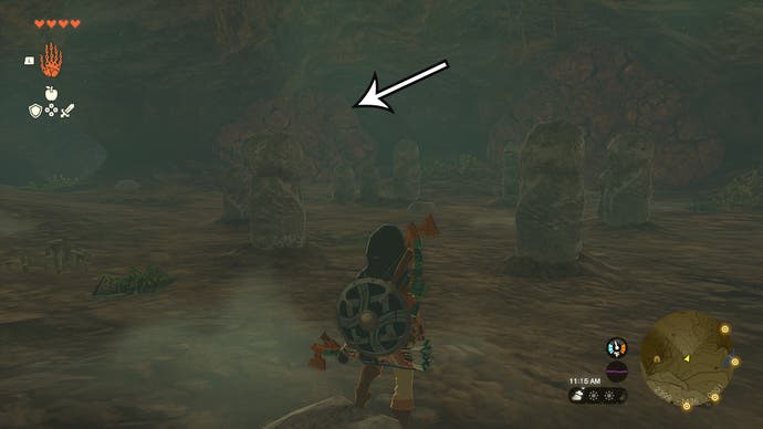 Link in a room with statues in the Robred Dropoff Cave, and an arrow pointing at rocks players need to destroy to head towards the Barbarian Helm.